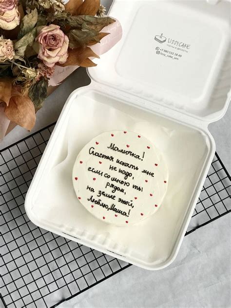 A Cake In A White Box With Writing On The Side And Flowers Next To It