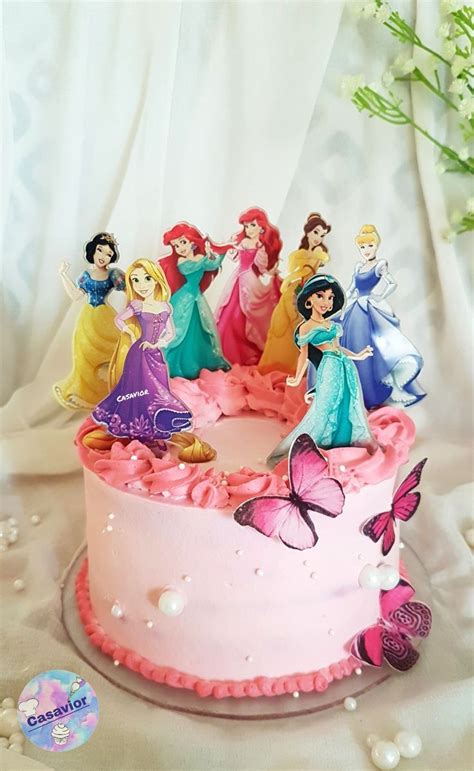 There Is A Pink Cake With Princess Figures On It And Flowers In The