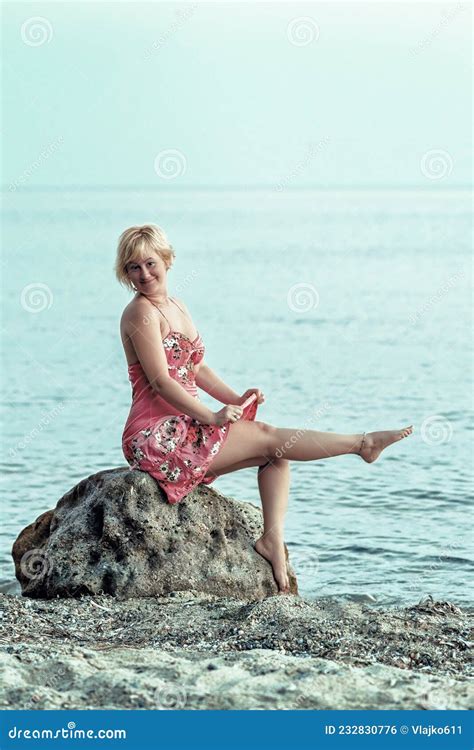 Happy Blonde Woman In A Reddish Flowered Dress Woman Sitting And Pose