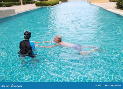 Happy Elderly Caucasian Husband And Elderly Asian Wife Swimming In Pool During Retirement