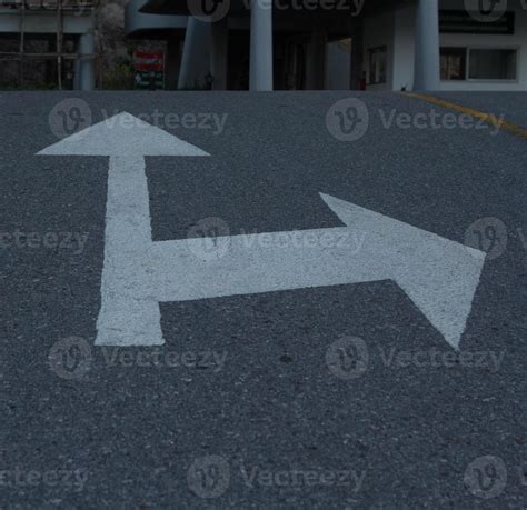 The White Arrow Traffic Sign On The Black Asphalt On The Road Is A