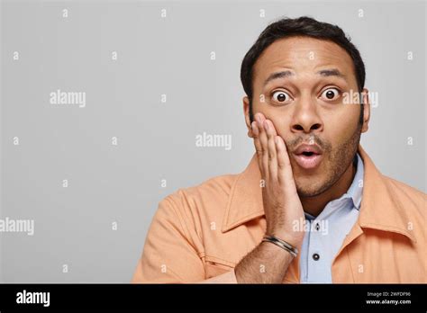 Shocked Handsome Indian Man In Orange Vivid Jacket Posing With Hand On