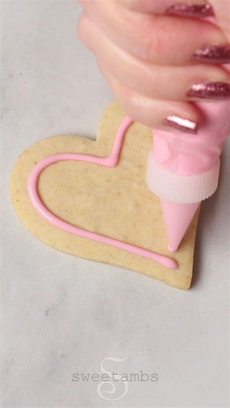 A Cookie Shaped Like A Heart Being Frosted By Someone S Hand With Pink