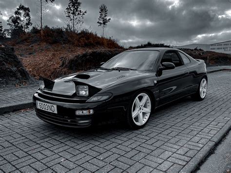 A Black Sports Car Parked On The Side Of A Road With Dark Clouds In The