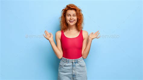 Positive Good Looking Girl With Ginger Hairstyle Spreads Hands Gets Awesome Surprise Has