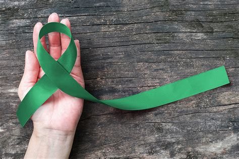 Liver Cancer Awareness ribbon Emerald Green color ribbon on human hand aged background, clipping ...