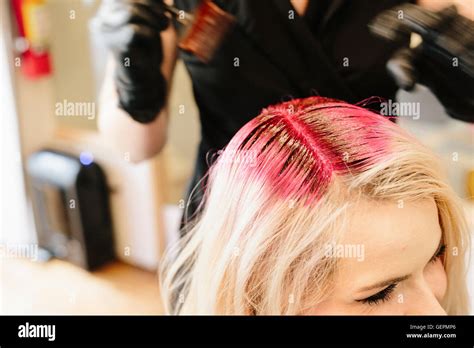 A Hair Colourist In Gloves Applying Red Hair Dye To A Clients Blonde