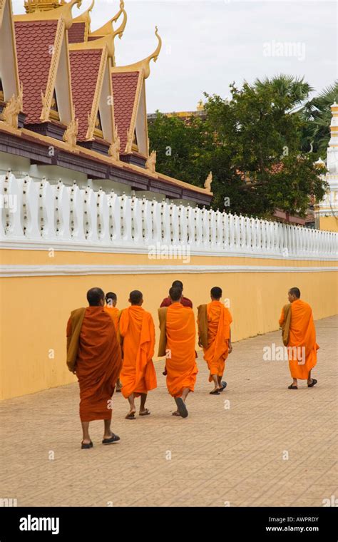 Buddhist Monks Dressed In Orange Robes Walk Along The Wall Of The Royal