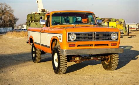 An Orange And White Truck Is Parked In The Dirt With Other Trucks