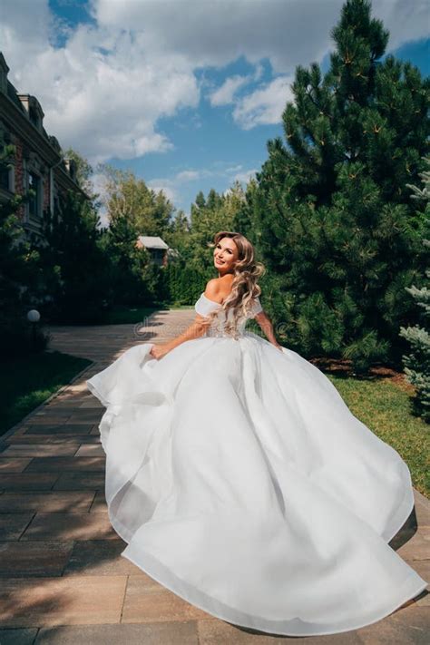 A Blonde Bride Running Down A Path In The Park In A White Long Dress