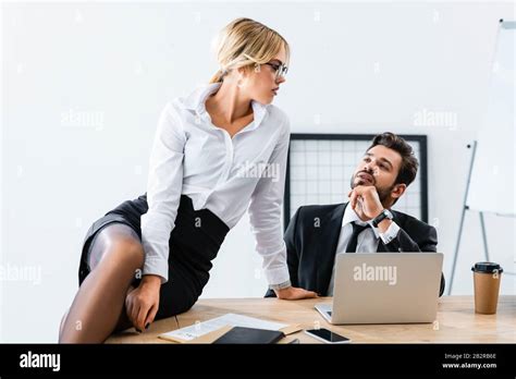 Sexy Secretary Sitting On Table While Flirting With Businessman Stock