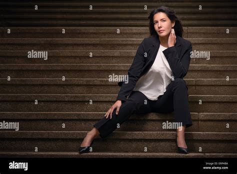 Attractive Brunette Woman In A Slack Suit Sitting On Urban Stairs Looking At Camera In A Sensual