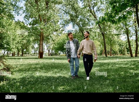 A Bearded Gay Couple Walks Hand In Hand Through A Lush Green Park