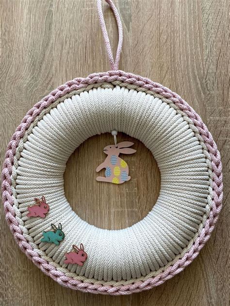 A White And Pink Knitted Wreath Hanging On A Wooden Floor With An