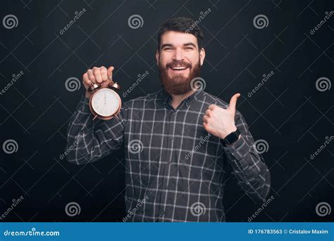 Portrait Of Cheerful Handsome Bearded Man Showing Alarm Clock Stock