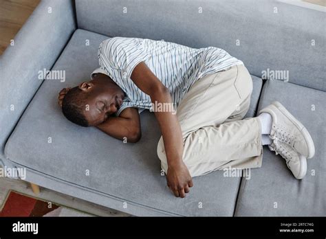 Top View Portrait Of Black Man Lying On Couch At Home Curled Up In