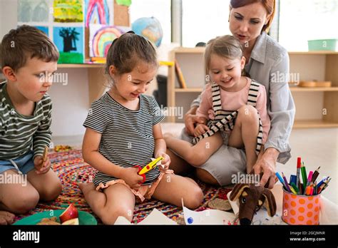 Group Of Small Nursery School Children With Teacher Sitting On Floor