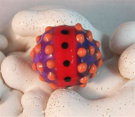 A Red And Purple Ball Sitting On Top Of White Rocks With Black Dots