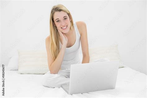 Content Blonde Woman Using Her Notebook Sitting On Her Bed Smili Stock Photo Adobe Stock