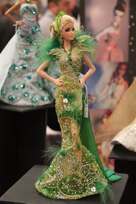 A Barbie Doll Dressed In Green And Gold Is Standing On A Black Stand