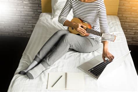 Happy Young Asian Woman Playing Ukulele Sitting On Bed In Bedroom