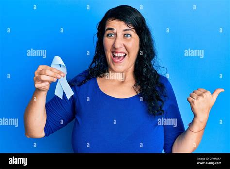 Plus Size Brunette Woman Holding Blue Ribbon Pointing Thumb Up To The