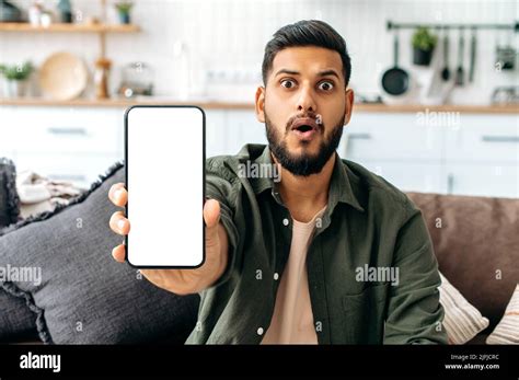 Surprised Amazed Indian Or Arabian Guy In Casual Wear Sits On Sofa In