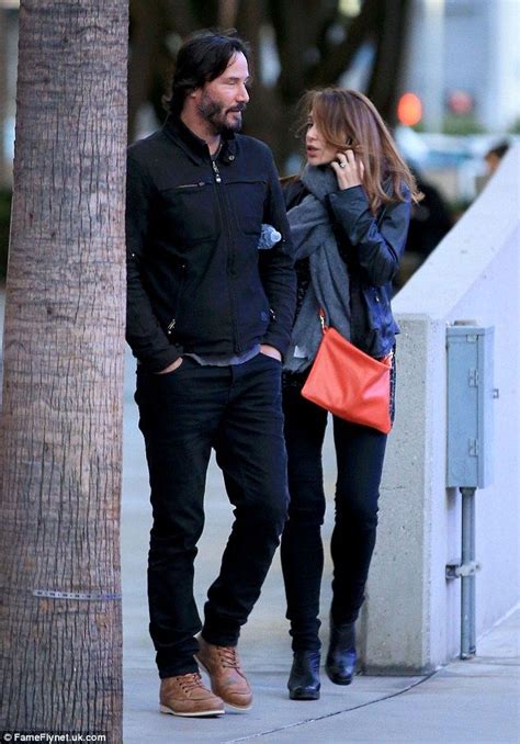 A Man And Woman Walking Down The Street Talking On Their Cell Phones