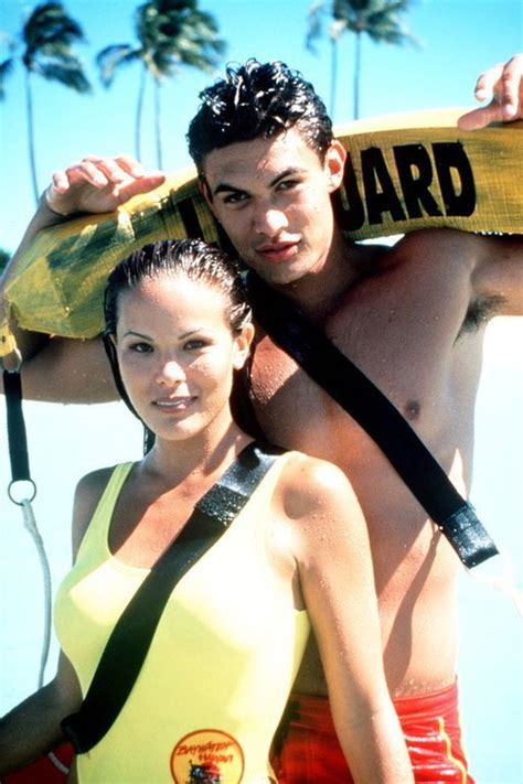 A Man And Woman Standing Next To Each Other On The Beach With