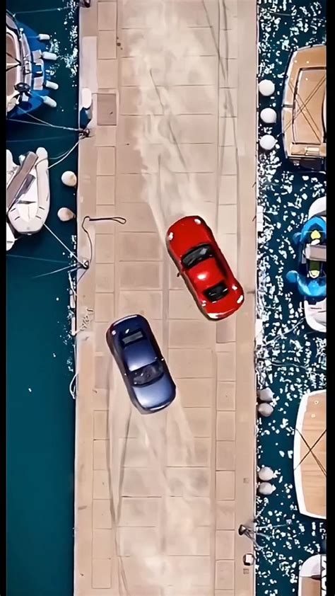 Two Cars Parked Next To Each Other In Front Of Some Boats On The Water