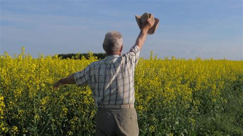 Elderly And White Haired Farmer In A Field Waving His Arms And Hat In