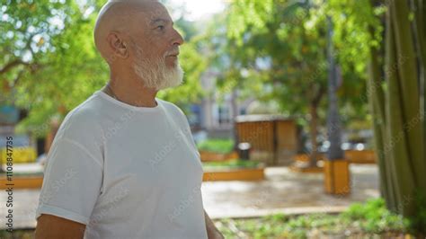 Mature Man Standing Outdoors In An Urban Park With Greenery In The