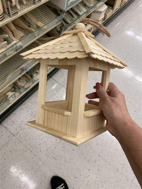 A Hand Holding A Wooden Bird House In A Store