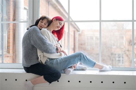 Two Women Dressed In Sweaters Sit By The Window And Gently Hug Lesbian