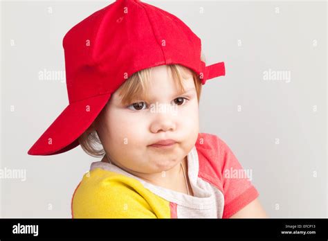 Studio Portrait Of Funny Confused Baby Girl In Red Baseball Cap Over