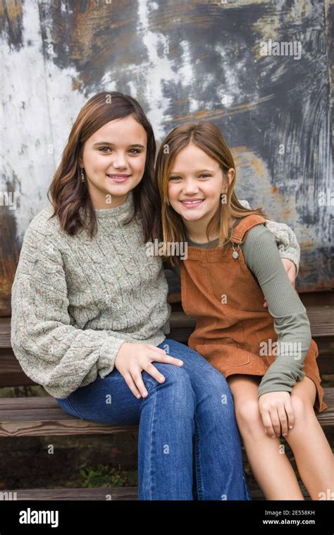 Two Young Sisters Sitting Next To Each Other And Hugging With Their Arms Around Each Other In