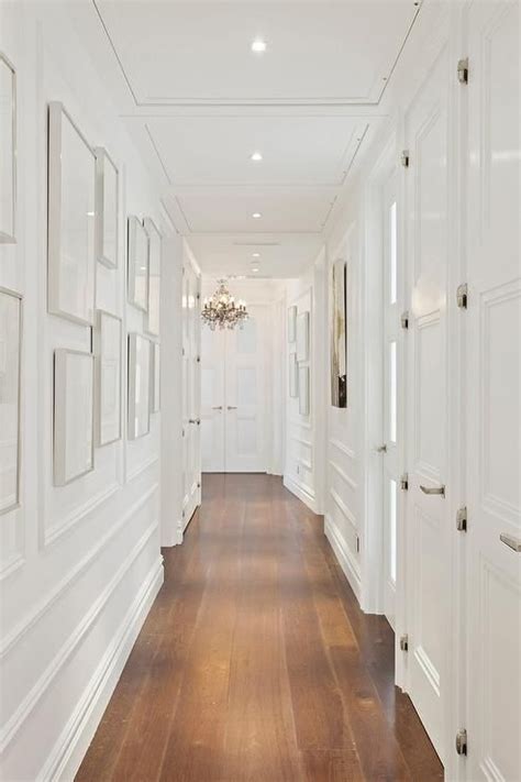 A Long Hallway With White Walls And Wooden Floors Framed Pictures On