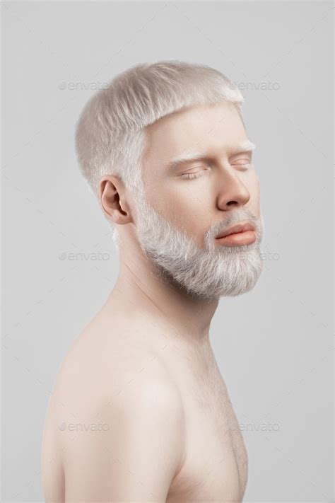 Peaceful albino man with closed eyes, pale skin and white hair posing against light grey ...