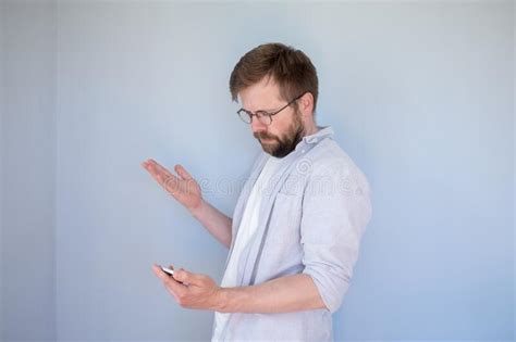 Puzzled Bearded Man In Glasses And Casual Clothes Looks At Smartphone