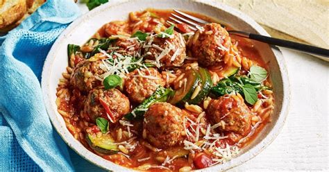 A White Bowl Filled With Meatballs And Pasta On Top Of A Blue Towel