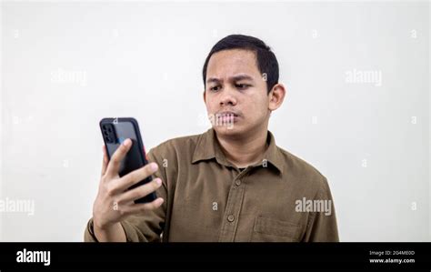 Young Asian Malay Man Looking At The Smartphone With A Serious And