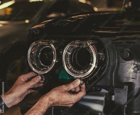 Car headlight in repair close-up. The car mechanic installs the lens in the headlight housing ...