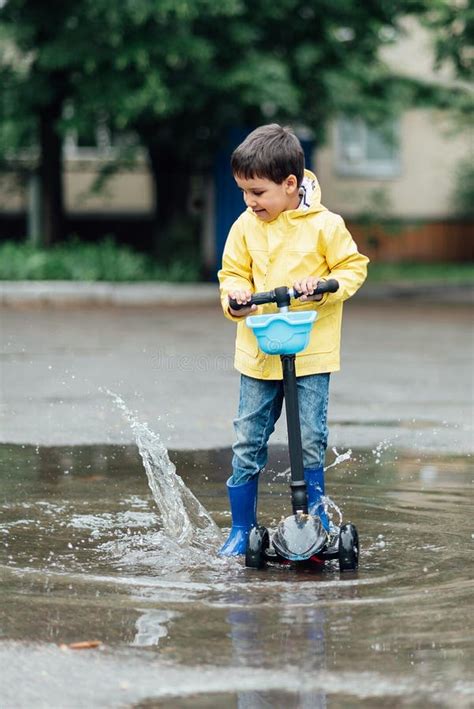 Little Boy In Raincoat And Rubber Boots Playing In Puddle Fun On