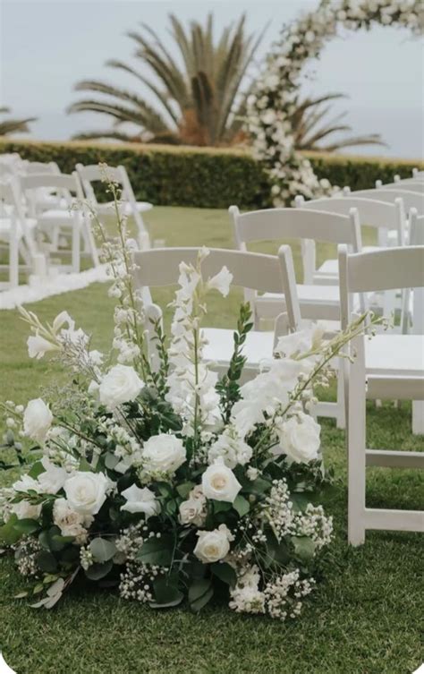 An Outdoor Ceremony Setup With White Flowers And Greenery On The Grass