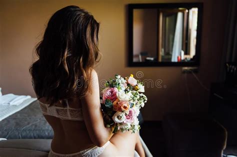 Beautiful Nude Brunette Bride With Bouquet And Wavy Hair Style In White Erotic Underwear Stock