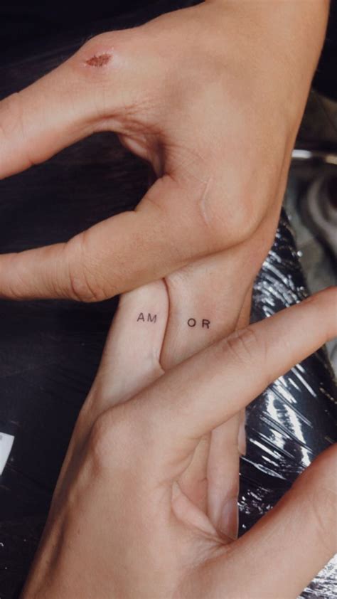 Two Hands Holding Each Other With Small Tattoos On Their Fingers And