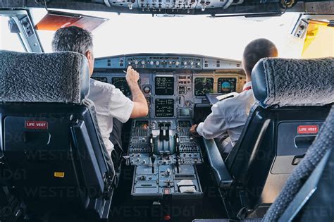 Back View Of Male Pilot And Co Pilot Using Instrument Panel In Cockpit