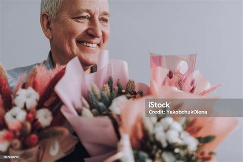 Happy Old Man Holding Beautiful Flowers While Standing Against White