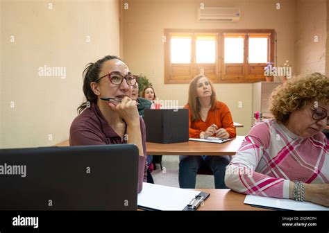 An Attentive Mature Woman Participating In A Classroom Lesson With Fellow Adult Learners Engaged
