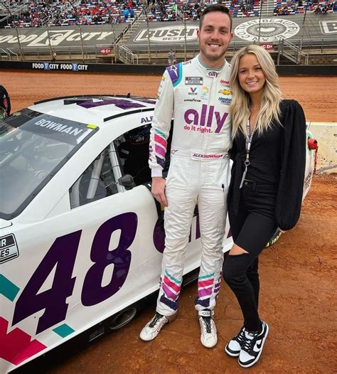 A Man And Woman Standing Next To A Race Car